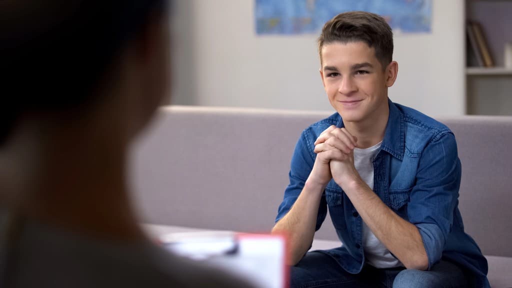 Teen sitting with a supportive therapist, feeling more at ease.
