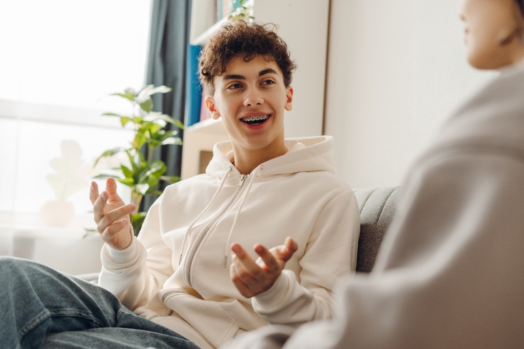 Warm, candid photo of a relieved-looking teenager sitting comfortably across from an empathetic therapist, natural window lighting, hopeful tone
