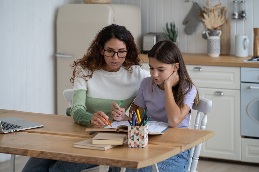 A worried but loving mother gently holding the hands of her stressed pre-teen child at the kitchen table, authentic emotional connection, soft focus