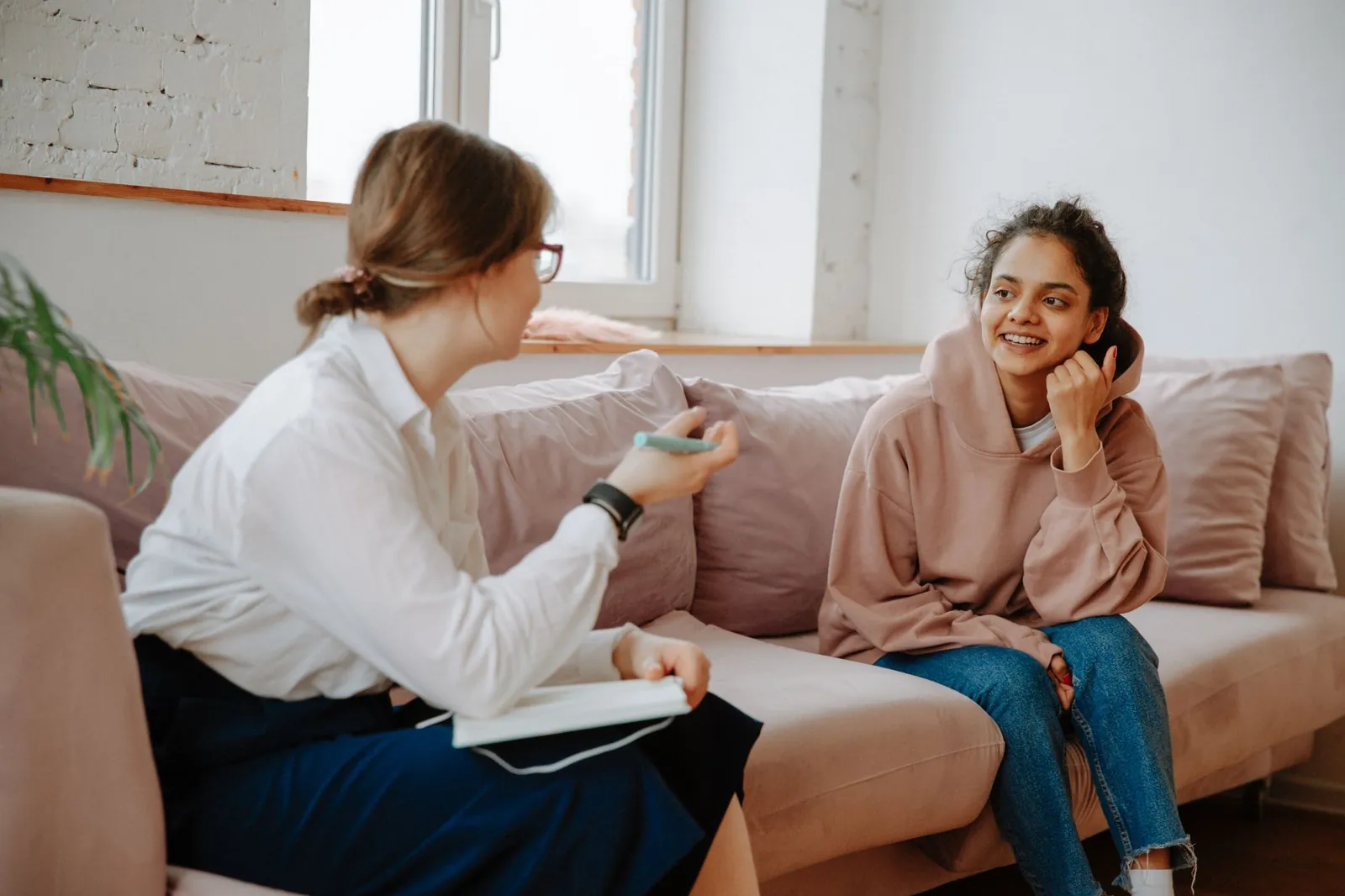 Smiling teenage girl in a hoodie talking with her therapist on a sofa