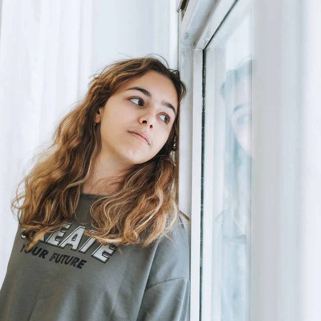 Teen girl looking out window. Trauma therapy in Thornhill, Vaughan for kids and teens near Markham and North York.