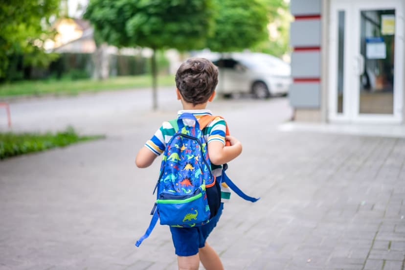 Young child wearing a backpack walking toward a school entrance, illustrating back-to-school anxiety Young child wearing a backpack walking toward a school entrance, illustrating back-to-school anxiety