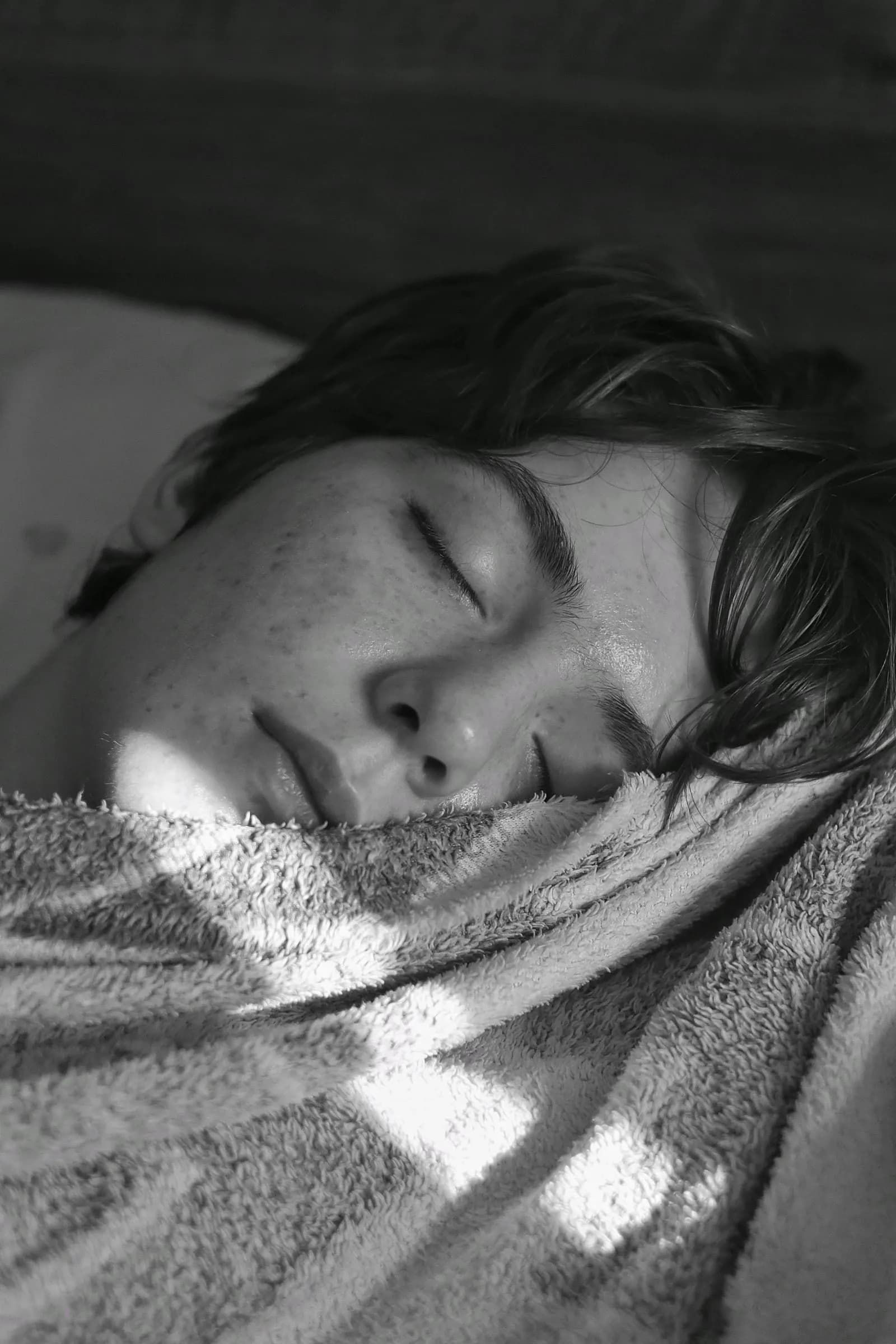 Teenager sleeping late under a heavy blanket on a dark winter morning, a common sign of seasonal depression