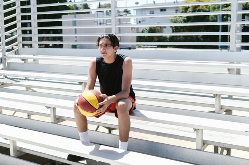 Teenage basketball player sitting alone on empty bleachers, managing pre-game nerves before a competition Teenage basketball player sitting alone on empty bleachers, managing pre-game nerves before a competition