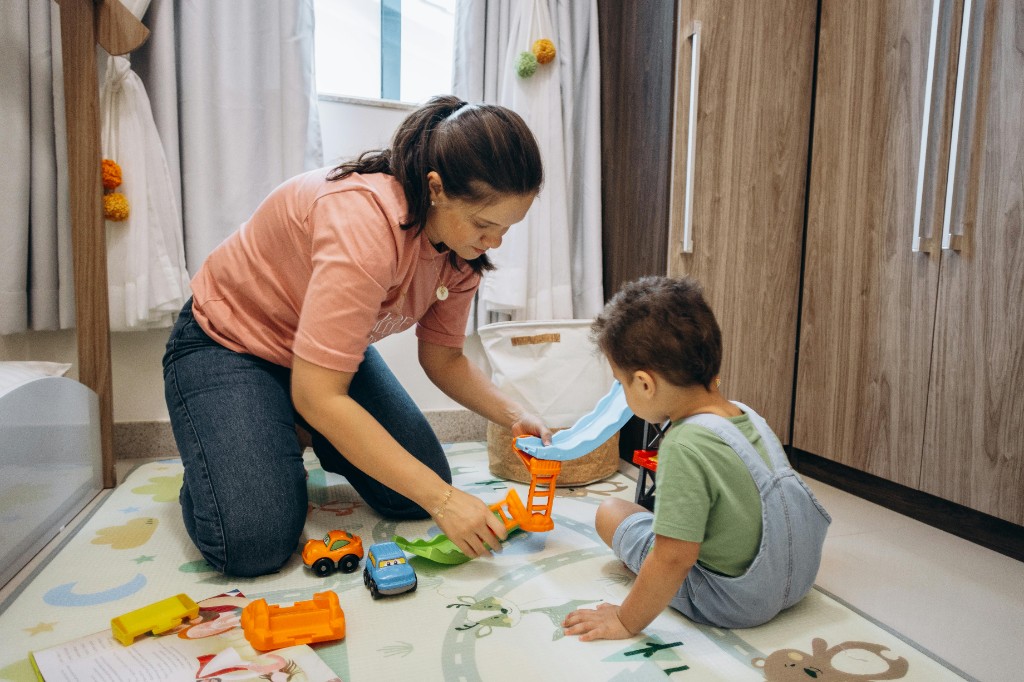 Parent and young child playing together with toy cars on a colourful play mat in a bright room, showing side-by-side connection and developmental play for child mental health.