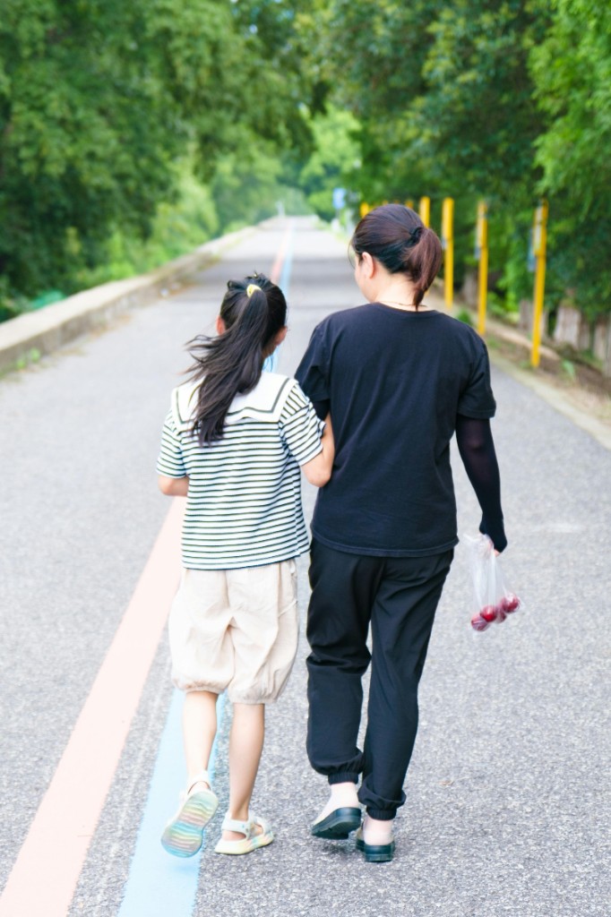 Parent and school-age child walking arm in arm down a tree-lined path, viewed from behind — symbolizing steady support, co-regulation, and emotional connection.