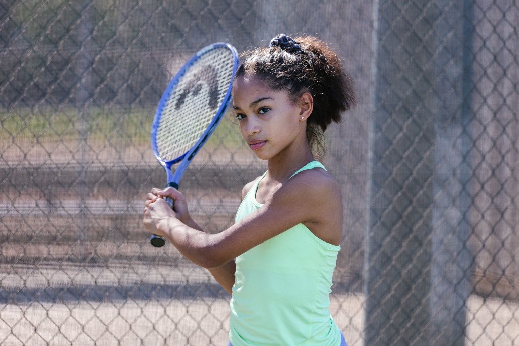 Young teen tennis player in ready stance gripping her racket on the court, illustrating focused pre-game readiness and a calm response to nerves