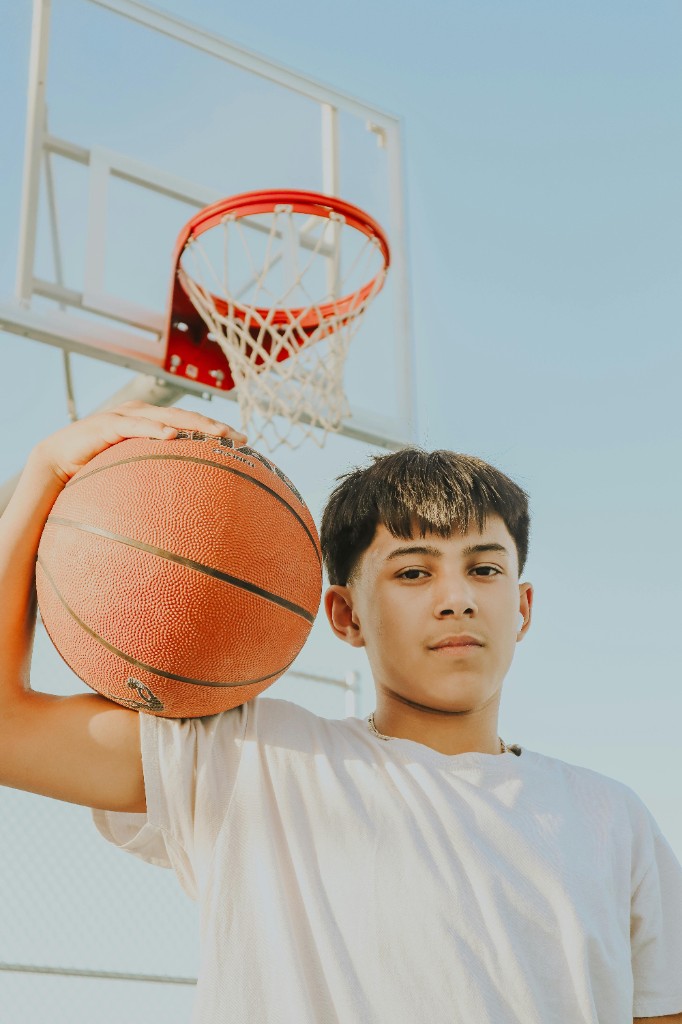 Teen basketball player standing confidently beside the hoop holding a ball, illustrating renewed self-confidence after therapy for sports performance anxiety
