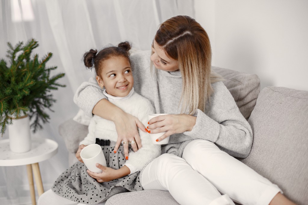Parent sitting calmly beside their child on a sofa in a quiet room after sensory overload, sharing a warm drink with low household noise, illustrating gentle post-meltdown recovery