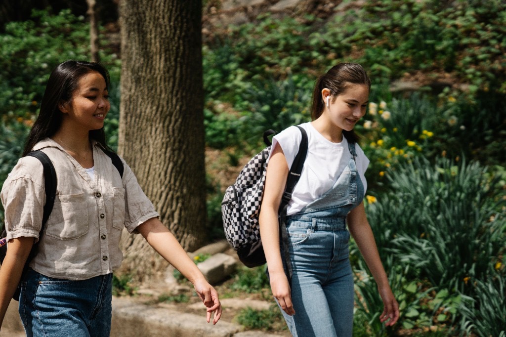 Two teenage friends walking outdoors together on a sunny tree-lined path, illustrating how movement, time outside, and staying connected support a teen's mental health day to day