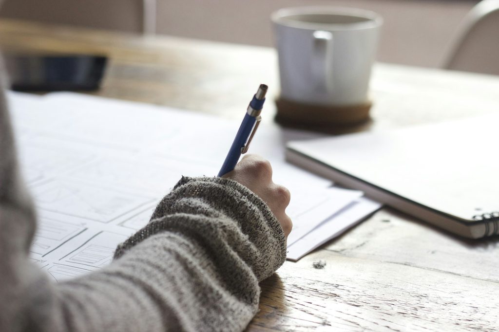 Close-up of a child's hand with a firm grip on a blue mechanical pencil while writing on lined paper at a wooden desk