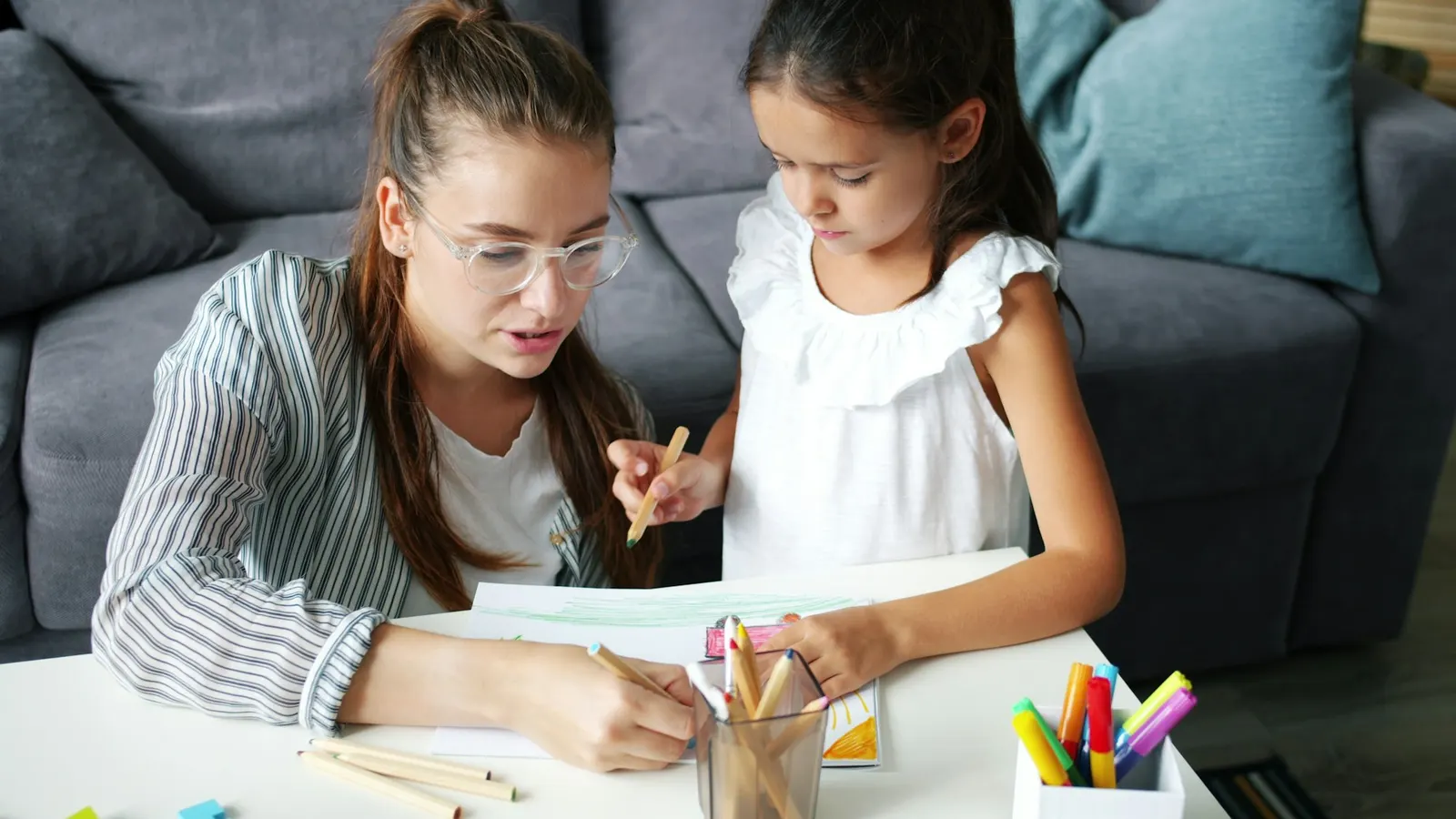 Parent sitting beside a child and asking about their drawing in a calm, curious way