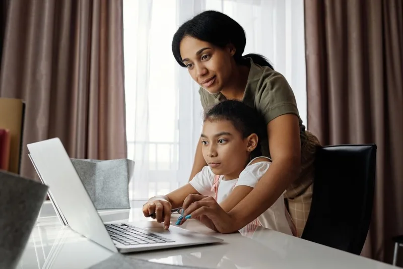 Parent sitting with a child at a laptop, offering calm support with schoolwork