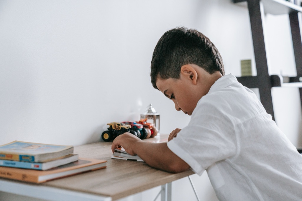 School-age boy slumped over his workbook at a desk at home, discouraged by a small mistake — a common sign of rejection sensitive dysphoria in children