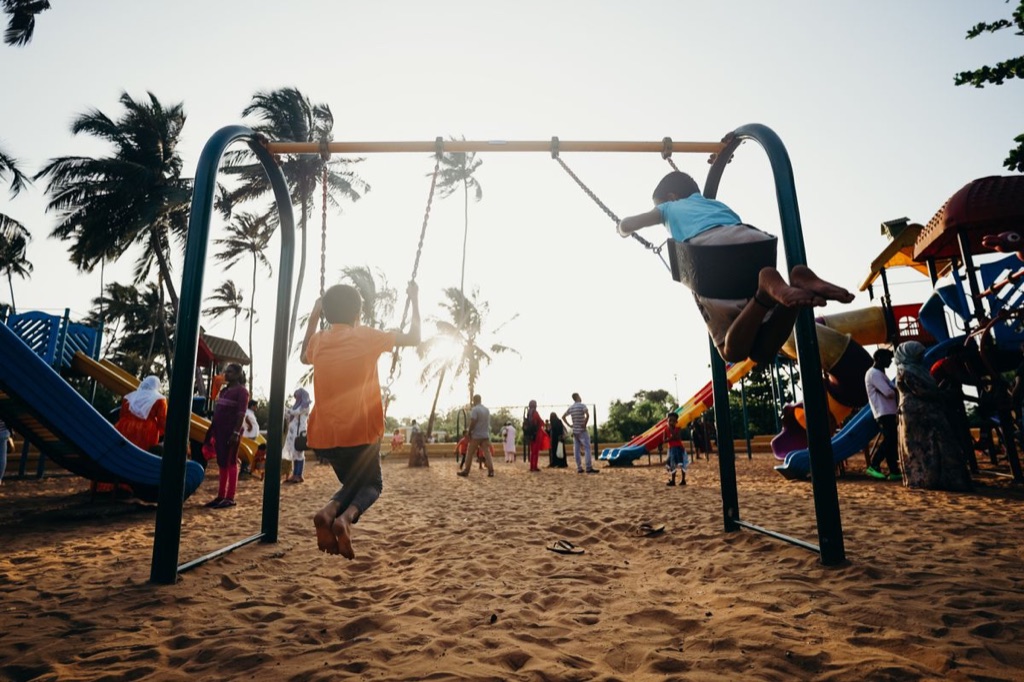 Two children swinging high on playground swings at sunset, enjoying the movement and play that sensory integration OT works toward