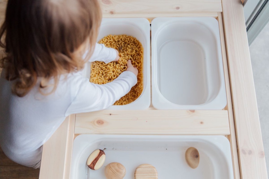 Young child exploring dry pasta with their hands in a sensory bin, a tactile activity used in pediatric occupational therapy