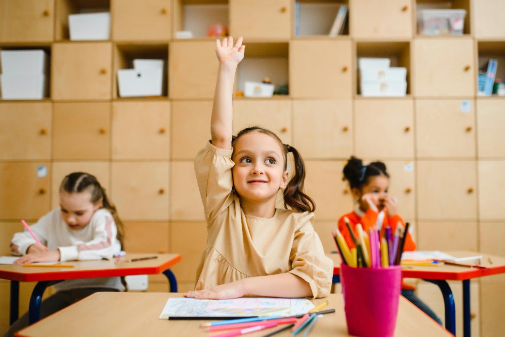 A girl raising her hand in a bright classroom — engaged on the surface in a way that can mask inattentive ADHD in girls
