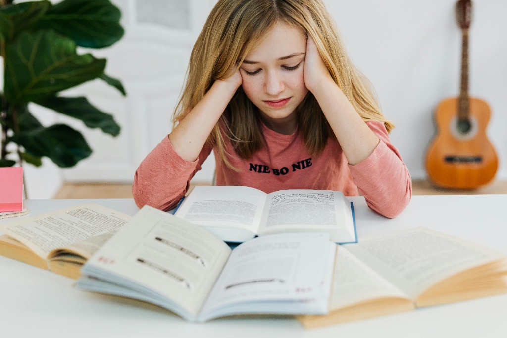 A young girl looking overwhelmed at her desk with several open books — when effort at school leaves nothing left for homework