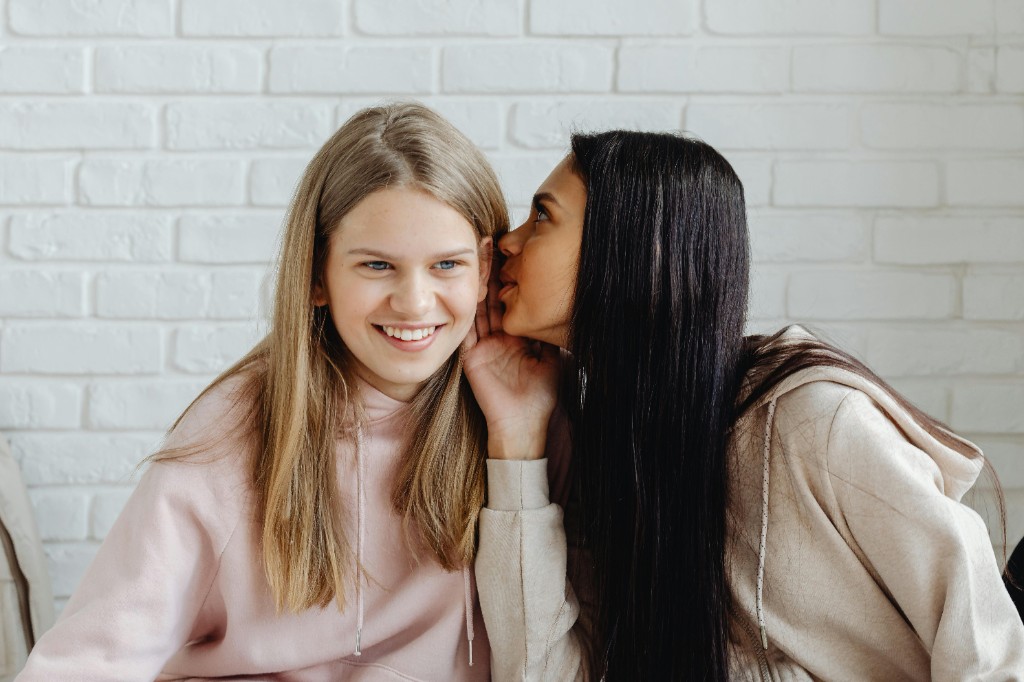 Two teenage girls whispering together — friendship intensity and social nuance often show up around ADHD in girls