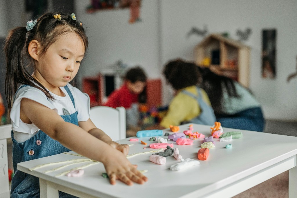 A young girl in a playroom carefully lining up strips of modelling clay in precise parallel rows — symmetry and ordering rituals are a common but missed sign of childhood OCD