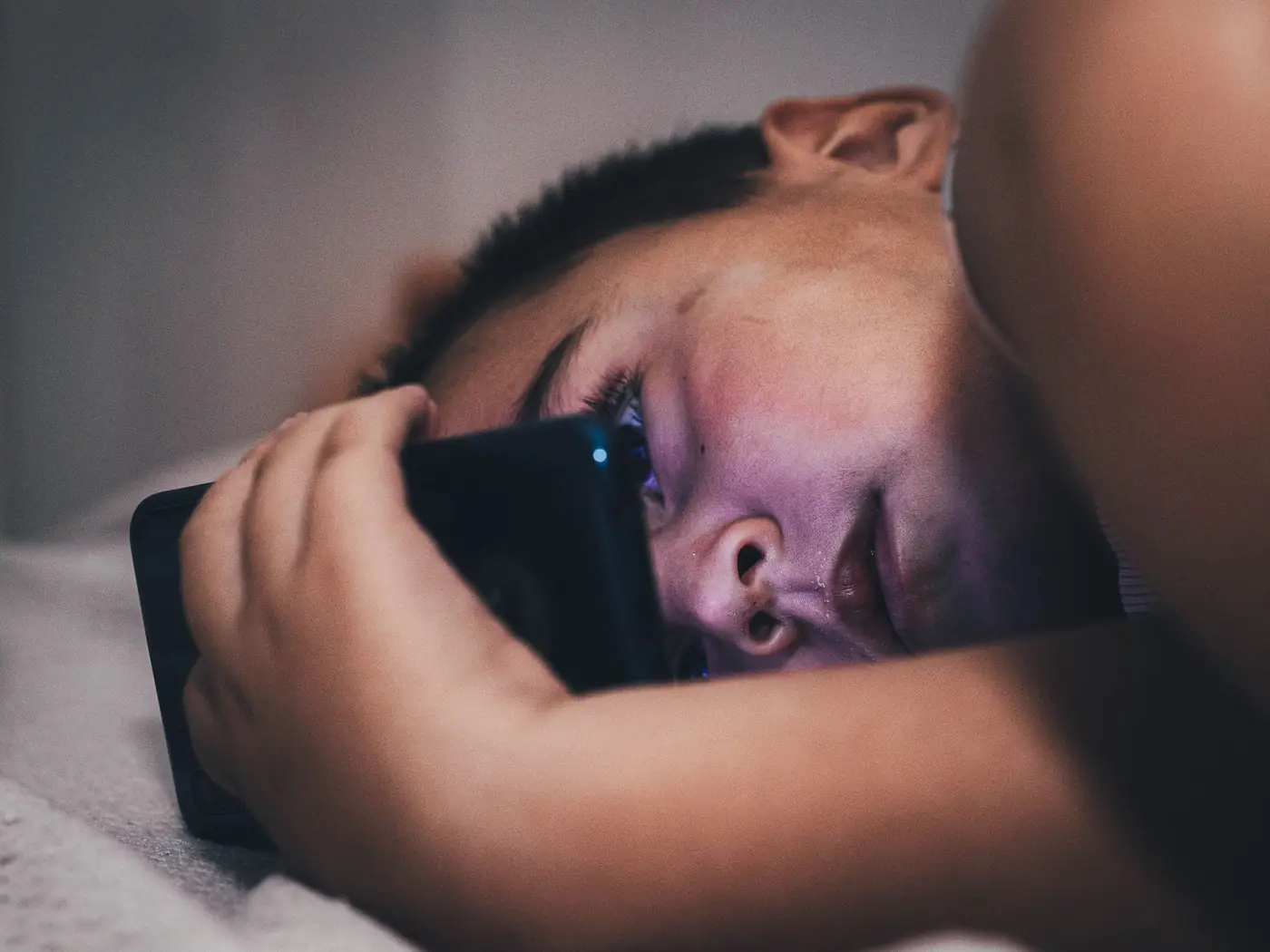 Teen looking at phone in bed at night, worried about cyberbullying messages