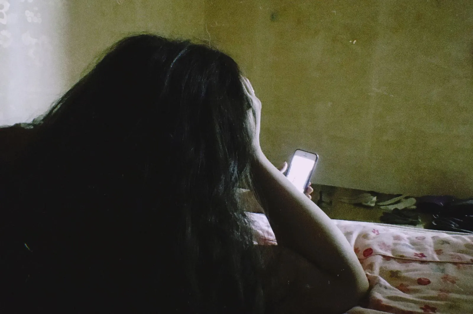 Withdrawn teen sitting alone in a dim bedroom in the evening, a possible sign of seasonal affective disorder