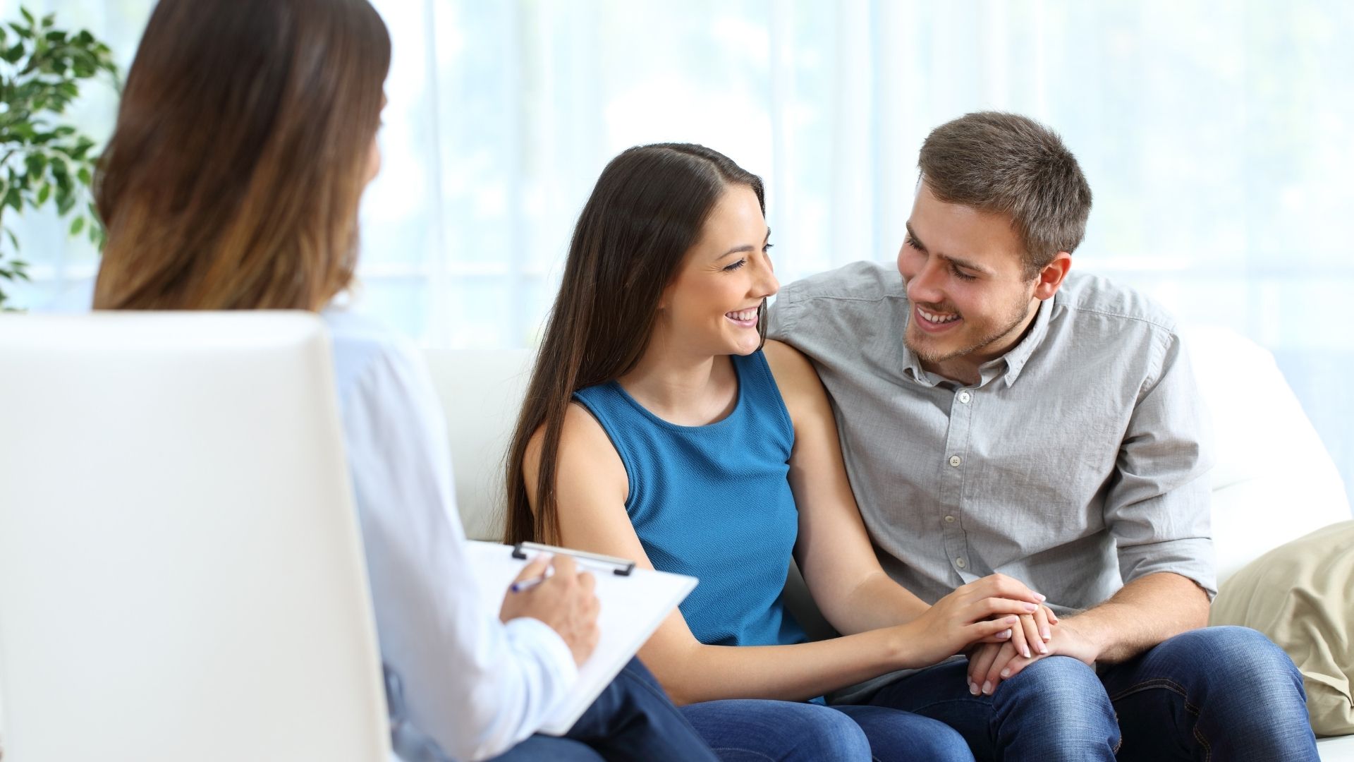 Couple in a therapy session with a therapist, smiling and holding hands.